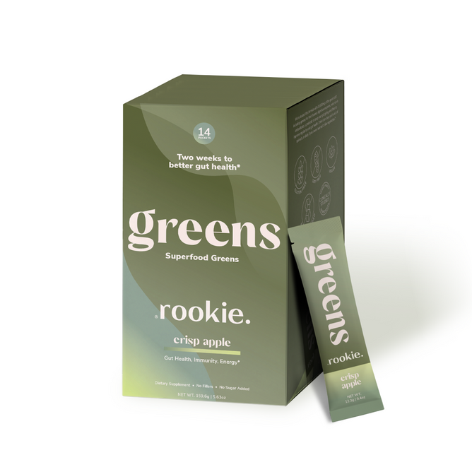 A green and olive Rookie Wellness Greens box labeled Superfood Greens in crisp apple flavor, shown with a single-serving stick pack. Highlights include daily fiber, immune-supporting antioxidants, and two weeks to better gut health.