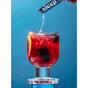 A hand pours Rookie Wellness Sleep Powder Packets, Relaxation & Sleep, into a glass of red drink with ice and lemon, set against a blue background.