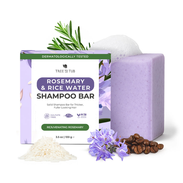 A lavender-hued Strengthening Shampoo Bar from Tree To Tub sits by its box, surrounded by rosemary, rice, coffee beans, and foam. This sulfate-free bar uses natural ingredients for a fuller-looking hair cleanse.