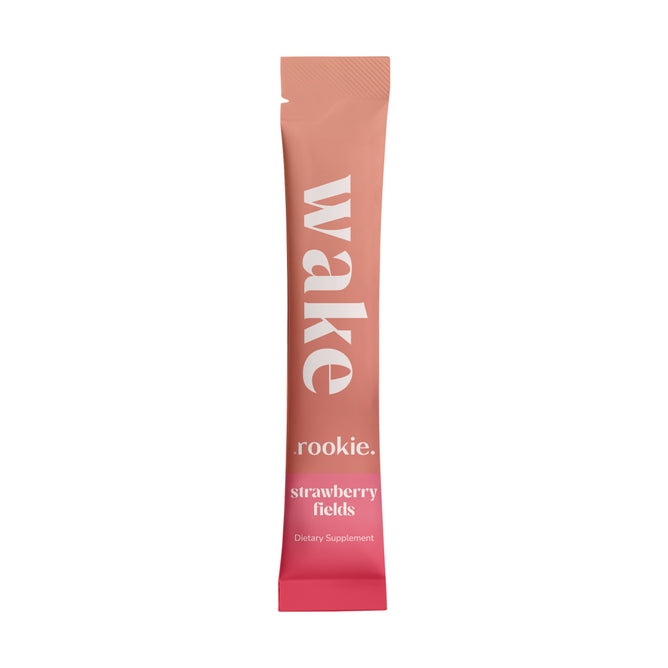 A single-serve pink packet labeled Rookie Wellness Wake Strawberry Fields - Sample Dietary Supplement stands upright against a white background, featuring energizing green tea for a natural lift.