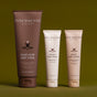 Three Innersense Organic Beauty Radiant Skin Ceremony body care products—Inner Glow Body Scrub (brown tube), Awaken Body Wash (light beige), and Renew Body Lotion (beige)—stand upright against an olive green background.