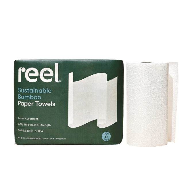 A package of Reel Premium Bamboo Paper Towels—135 2-ply sheets per roll—sits beside a single white roll, with green packaging and white text emphasizing these sustainable, tree-free towels.