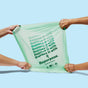 Three hands stretch a pale green Repurpose Compostable Tall Kitchen Bag, Lavender Scented, against a light blue background. The bag displays "Replace it with Repurpose," brand logo, and compostable certification icons.