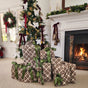 Reusable Gift Bags Set - 100% Cotton from Waste Free Celebrations, along with plaid-wrapped presents tied with green ribbons, are stacked near a fireplace. A decorated Christmas tree and wreath complete the cozy, festive living room décor.