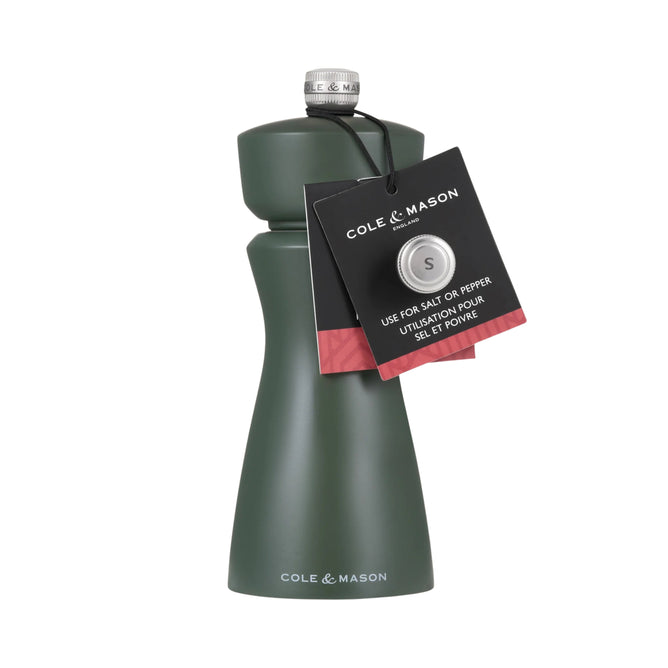 A dark green Cole & Mason 2-in-1 Kenton Salt & Pepper Mill with a silver top features a ceramic grinder. A black tag on the neck shows the brand name and provides instructions for using the ceramic mechanism.