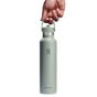 A hand holds a green Hydro Flask Standard Mouth Bottle with Flex Straw Cap, 24 oz, featuring TempShield double-wall insulation. The sleek design and logo keep drinks perfectly hot or cold, standing out against the plain white backdrop.