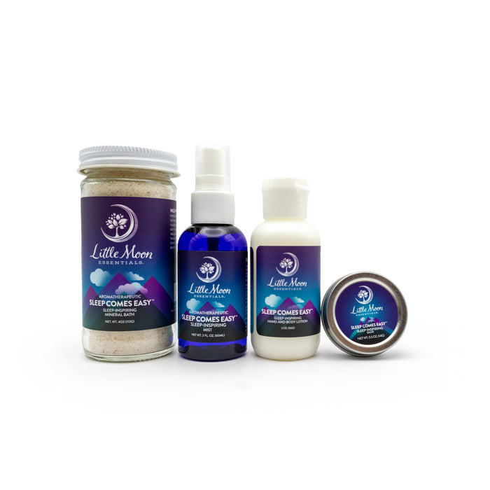 The Sleep Comes Easy Gift Set by Little Moon Essentials is displayed on a white background, featuring calming products: mineral bath salts in a jar, a blue spray bottle, a lotion bottle, and a small tin. Each has a purple Sleep Comes Easy label to promote restful sleep.