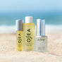 The OSEA Vagus Nerve Travel Set is displayed upright on sandy beach with a blurred ocean and sky, evoking relaxation and making it the perfect wellness companion for your next getaway.