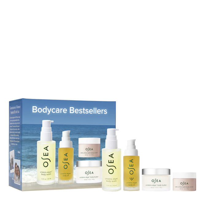 OSEA’s Bodycare Bestsellers Set includes five top skincare products, such as the Undaria Algae Body Oil, all in travel-sized bottles and jars with signature white and yellow labels, displayed before a blue ocean-themed box.