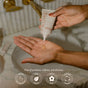 A hand squeezes a drop of Renewing Hand Serum from a small tube onto the palm of another hand, with four circular icons below listing the product benefits and certifications.