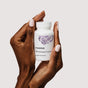 Two hands with light pink nail polish hold a white bottle labeled "Thorne Perimenopause Complete Capsules" for perimenopause support and mood balance, featuring a purple floral design on a plain light background.