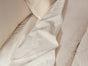 A close-up of unmade cream and white bed linens, featuring Coyuchi’s Organic Crinkled Percale™ Sheet Set, a textured blanket, and pillows.
