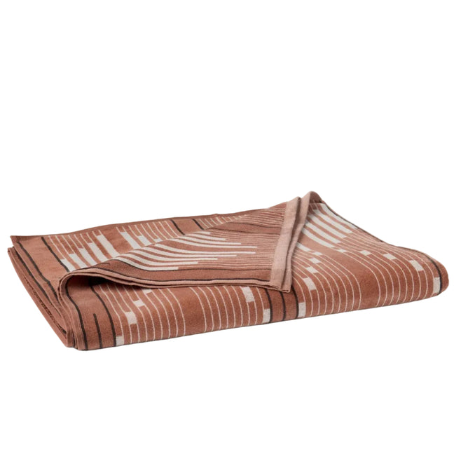 The Coyuchi Morelia Organic Beach Towel, featuring a folded brown design with a white and black geometric striped pattern inspired by ikat textiles, is displayed on a plain white background.