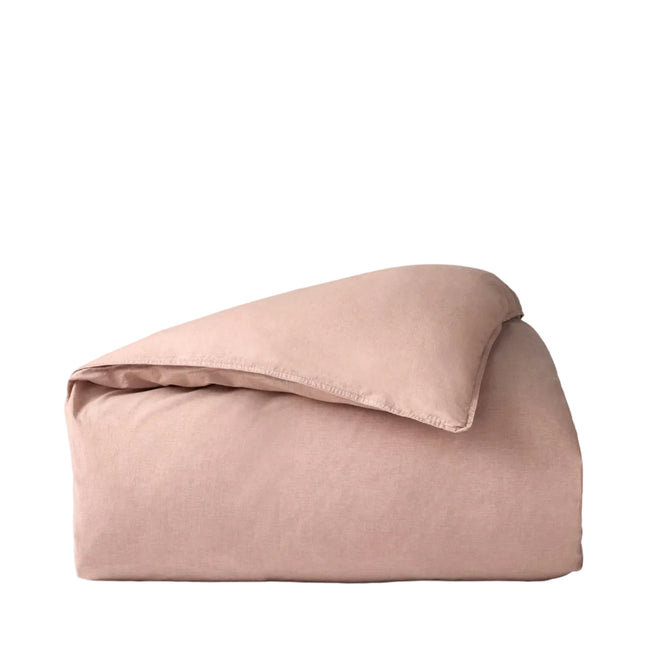 A neatly folded blush pink comforter with a smooth texture, set against a plain white background, highlights the elegance of the Coyuchi Organic Crinkled Percale™ Duvet Cover—crafted from breathable, luxurious organic cotton.