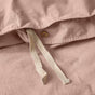 Close-up of the Coyuchi Organic Crinkled Percale™ Duvet Cover in light pink, featuring a white tie and a brown button at the opening. The organic cotton fabric showcases a soft, slightly wrinkled crinkled percale texture for superior breathability and comfort combined with stylish design.