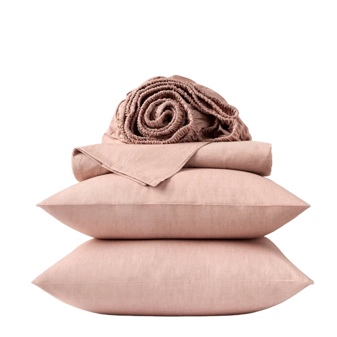 Two pink pillows stacked with a folded and rolled pink quilt on top, all set against a plain white background—an inviting arrangement that highlights the Coyuchi Organic Crinkled Percale™ Sheet Set, crafted from breathable GOTS certified cotton for ultimate comfort.