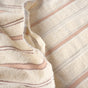 A close-up of the Coyuchi Acacia Organic Hand Towel, Set of 2, in beige, featuring thin brown and gray textured stripes. The towel’s soft, absorbent fabric is slightly wrinkled, highlighting its gentle texture and neatly folded edge.
