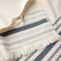 A close-up of the Coyuchi Aptos Organic Hand Towel, Set of 2, featuring cream-colored woven organic cotton with blue and gray stripes and fringed edges, displayed on a flat surface.