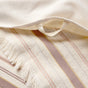 Close-up of a cream-colored woven fabric with beige, yellow, and brown stripes, featuring fringed edges and a sewn-in hanging loop. The Aptos Organic Hand Towel, Set of 2 by Coyuchi is crafted from organic cotton for quick drying and everyday convenience.
