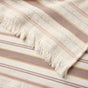 A close-up of the Aptos Organic Hand Towel Set of 2 by Coyuchi showcases two cream-colored textiles woven from soft organic cotton, each adorned with horizontal stripes in beige, brown, and yellow tones and finished with fringed edges. These absorbent towels are perfect for adding a stylish decorative touch to your kitchen.