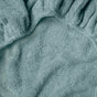 Close-up of the Coyuchi Cloud Loom™ Organic Changing Pad Cover in soft, light teal, featuring gathered elastic edges, textured fabric, and curved stitching.