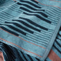 A close-up of the Morelia Organic Beach Towel by Coyuchi, featuring absorbent cotton in blue, black, and orange wavy and striped patterns, with a corner folded over the main fabric.