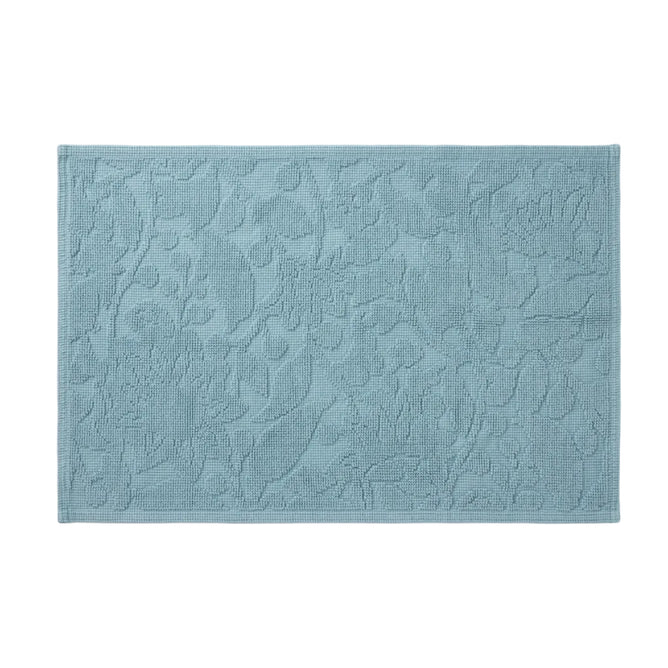 Coyuchi’s Wildflower Organic Bath Rug in light blue features a rectangular shape with an embossed floral pattern and textured surface, displayed against a white background.