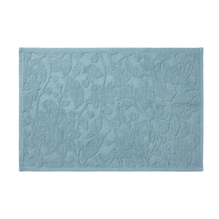 Coyuchi’s Wildflower Organic Bath Rug in light blue features a rectangular shape with an embossed floral pattern and textured surface, displayed against a white background.