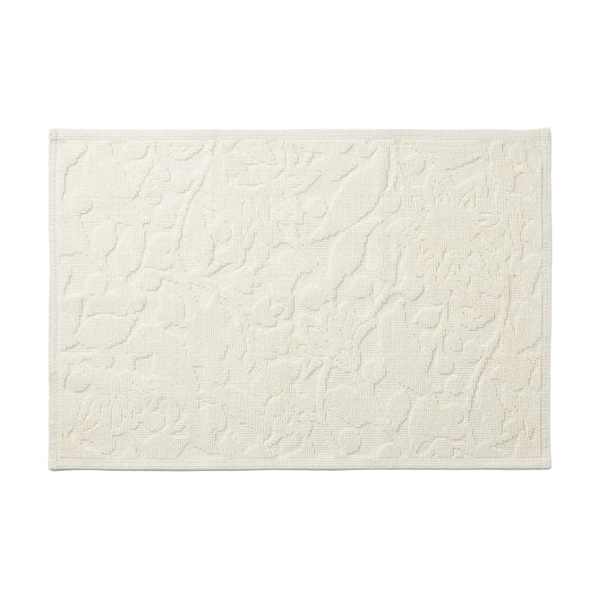 The Wildflower Organic Bath Rug by Coyuchi is a rectangular, off-white, textured absorbent bath mat featuring raised abstract patterns and a subtle border, shown on a white background.