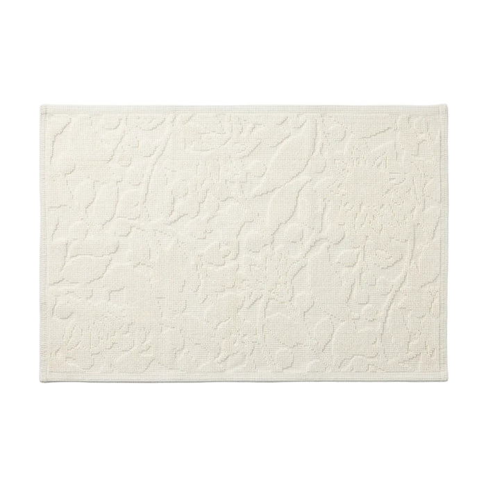 The Wildflower Organic Bath Rug by Coyuchi is a rectangular, off-white, textured absorbent bath mat featuring raised abstract patterns and a subtle border, shown on a white background.
