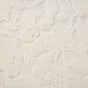 A close-up of the Coyuchi Wildflower Organic Bath Rug reveals a cream-colored, textured surface with a raised mid-century floral motif crafted from small, densely packed loops, evoking the feel of an absorbent bath mat.