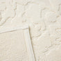Close-up of the Coyuchi Wildflower Organic Bath Rug in a textured, off-white organic cotton, shown with a folded corner to display the intricate pattern and the underside.