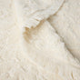 A close-up of the Coyuchi Wildflower Organic Bath Towel, featuring a cream-colored textured weave with a subtle botanical pattern reminiscent of florals, reversible design, and fringed edges, partially folded on a flat surface.