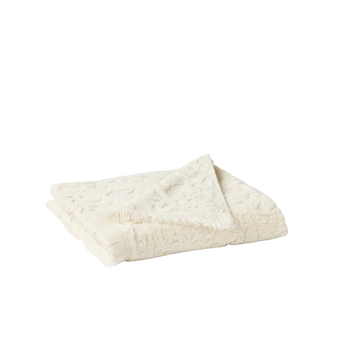 The Coyuchi Wildflower Organic Bath Towel, crafted from cream organic cotton with a tufted floral texture and fringe trim, is shown folded on a white background.