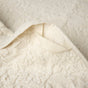 A close-up of the Coyuchi Wildflower Organic Bath Towel showcases its textured, cream-colored organic cotton fabric, with a small fabric loop visible on the underside. The towel’s material appears soft and patterned, reflecting both comfort and quality craftsmanship.