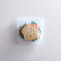 A sandwich with lettuce, tomato, and optional cheese or meat is stored in a Stasher Reusable Silicone Sandwich Bag (2-pack), shown on a light textured surface.