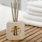 An Enviroscent Stix Diffuser Air Freshener Starter Kit - Pet Odor Neutralizer with three paper-like sticks in a wooden stand, sitting on a slatted wood surface next to a stack of white towels.