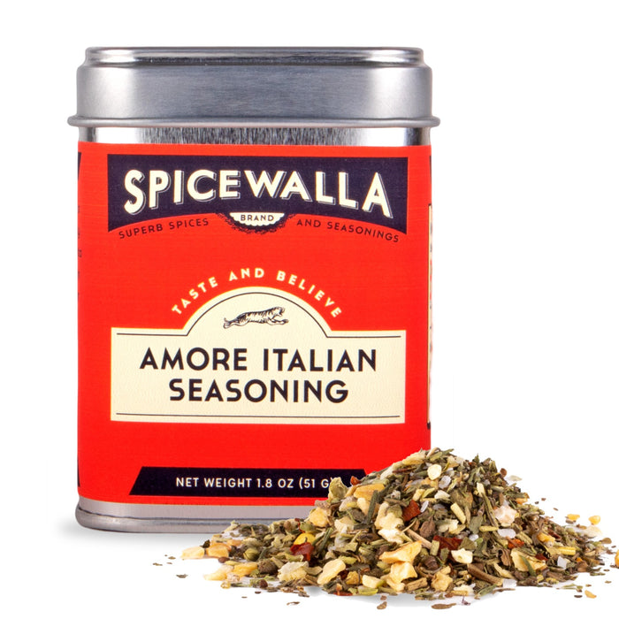 A red and cream Spicewalla Amore Italian Seasoning tin sits behind a small pile of dried herbs and spices on a white background.