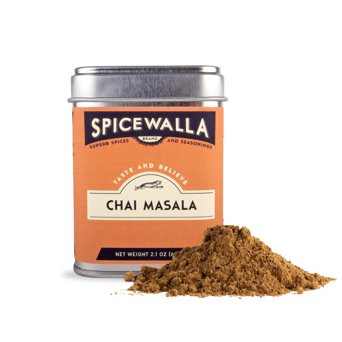 A Spicewalla Chai Masala tin sits beside a small mound of loose chai masala powder, showcasing this aromatic Indian spice blend against a white background.