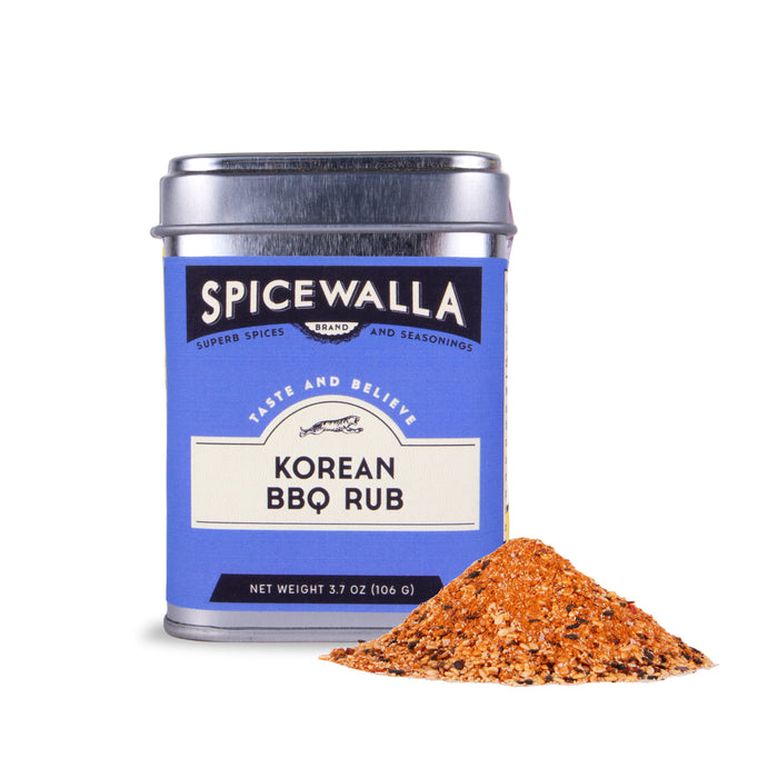 A Spicewalla Korean BBQ Rub tin with a blue label and silver lid is pictured alongside a small pile of reddish-brown spice mix, featuring gochugaru chili flakes and sesame seeds.
