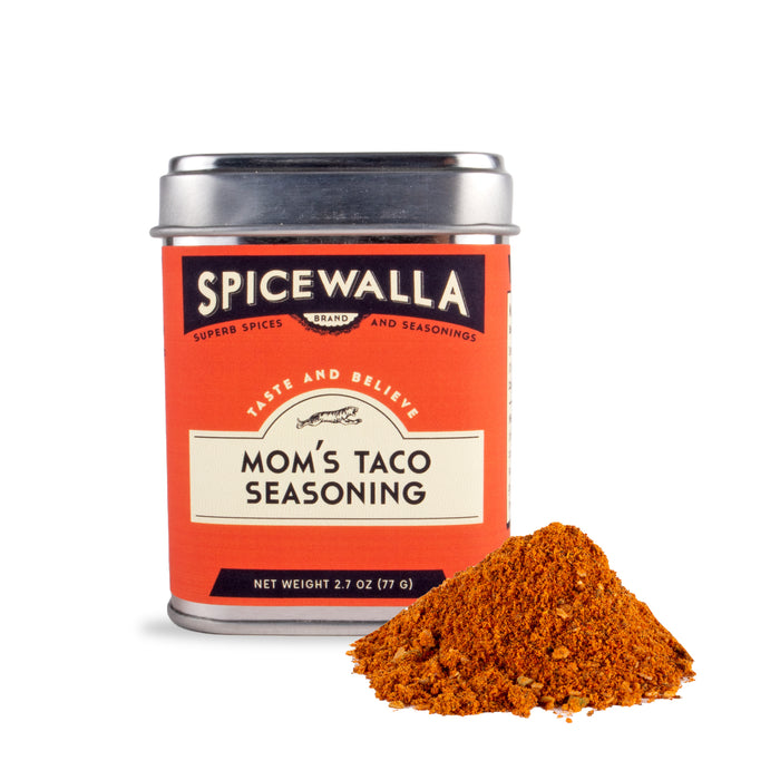 A tin of Spicewalla Moms Taco Seasoning sits beside a small heap of reddish-brown taco spice. The tin features a vibrant red and orange label.