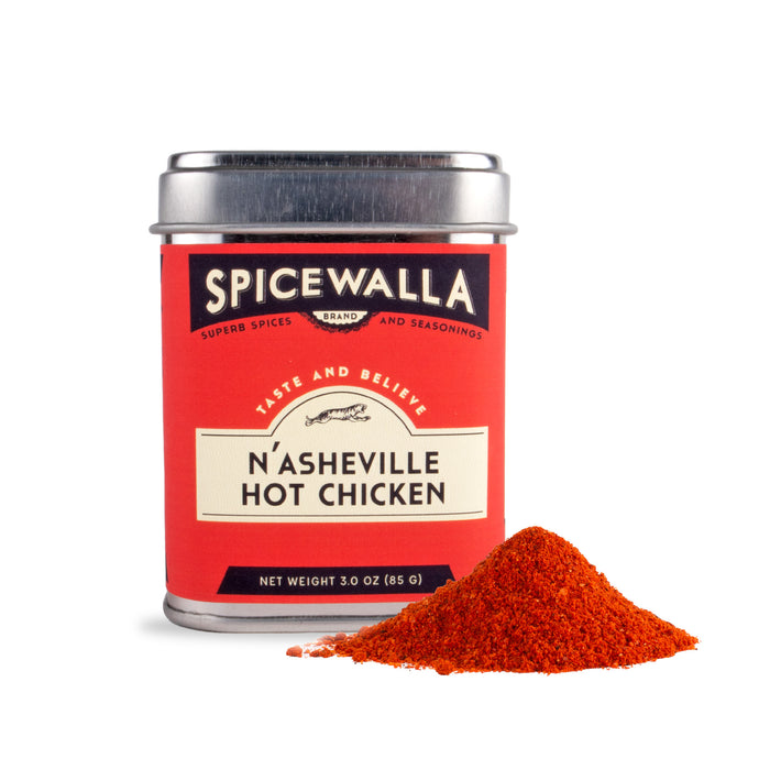 A Spicewalla NAsheville Hot Chicken tin sits beside a fiery red-orange pile of ultra-spicy seasoning, perfect for crispy fried chicken inspired by Asheville, NC, all set on a white background.