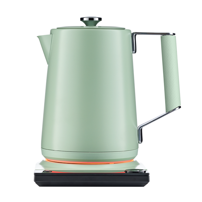 The SAKI Luna Electric Kettle Pro in matte green, featuring a textured handle, rests on a sleek white and black base, with an illuminated orange ring showing it’s powered on. Designed for convenience, its preset programs and adjustable temperature settings ensure perfect brewing for your favorite drinks. The background is plain white.