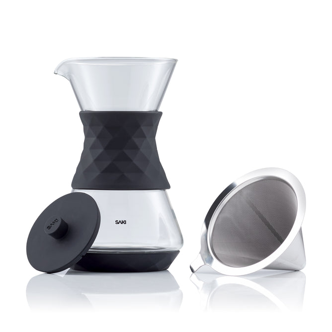 The Saki Pour-Over Glass Coffee Maker features borosilicate glass, a black silicone grip, and comes with a matching black lid. A separate reusable coffee filter is placed beside it.