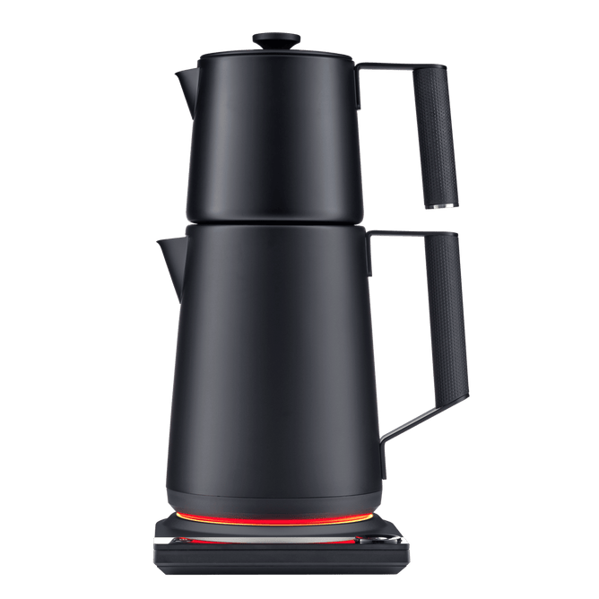 The SAKI Turkish Tea Maker Pro, a modern black electric kettle featuring a unique double-stacked pot design, sits on a base with an orange glowing ring. It offers convenient temperature control, making it perfect for preparing Turkish tea, and is photographed against a plain white background.