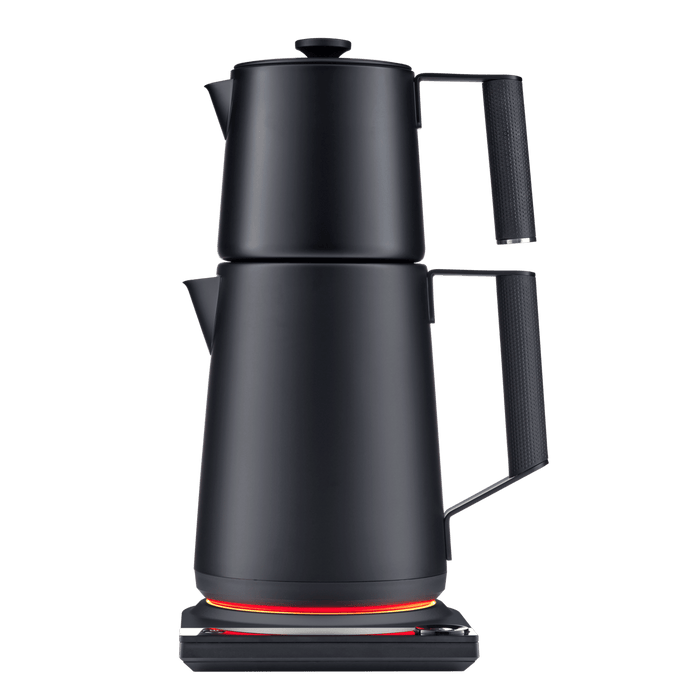 The SAKI Turkish Tea Maker Pro, a modern black electric kettle featuring a unique double-stacked pot design, sits on a base with an orange glowing ring. It offers convenient temperature control, making it perfect for preparing Turkish tea, and is photographed against a plain white background.