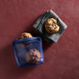 Two chocolate chip cookies sit on a gray napkin beside a blue Stasher Reusable Silicone Sandwich Bag 2-pack, filled with more cookies, on a red surface. These dishwasher-safe bags keep your snacks fresh and are ideal for treats.