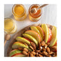 Sliced apples with almonds and pecans are arranged on a wooden board, surrounded by three jars from the Honey Artisanal Sampler Set by Savannah Bee Company—featuring Lavender, Acacia, and Orange Blossom honey—each paired with its own honey dipper. The scene is bright and inviting.