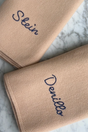 Two tan superfine merino The Sawa - Henna baby blankets, each embroidered with a different name in dark thread.