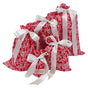 Five festive red and white patterned gift bags from the Waste Free Celebrations Reusable Gift Bags Set—crafted from 100% cotton—are displayed in a charming arrangement, each tied with a large, elegant white satin ribbon bow. A small Waste Free Celebrations tag is attached to the smallest bag at the front, showcasing these beautiful bags as an eco-friendly and sustainable alternative to traditional gift wrap for any special occasion.